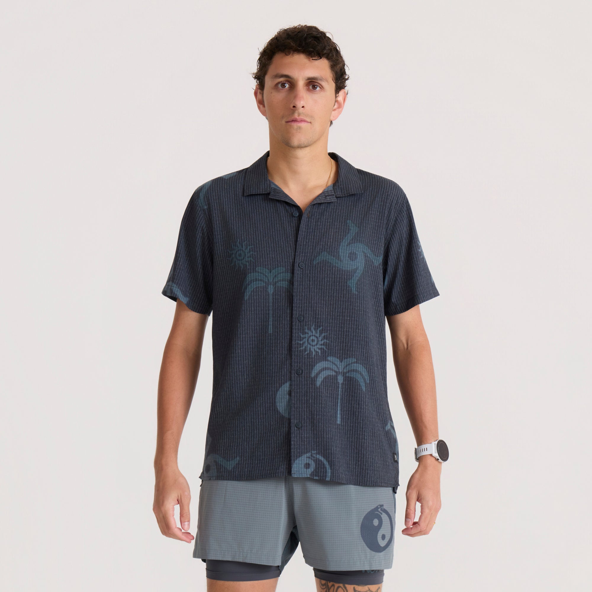 Bless Up Trail Button Up Shirt in ebony with palm tree print, worn by man with gray shorts on neutral background